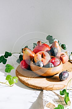 Assorted fruits in a wooden plate on a marble background, green ivy mango, peach, plum, pear, pomegranate