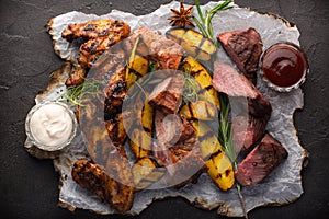 Assorted grilled meat and potatoes on black background
