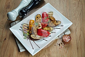 Assorted grilled vegetables - mushrooms, zucchini, peppers in a ceramic plate on a wooden background. Vegetarian warm salad.