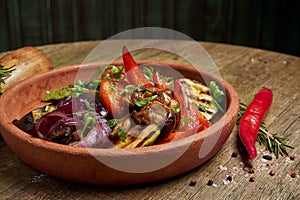 Assorted grilled vegetables - mushrooms, zucchini, peppers, corn in a ceramic plate on a wooden background. Vegetarian warm salad