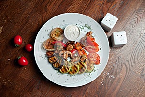 Assorted grilled vegetables - mushrooms, zucchini, peppers, corn in a ceramic plate on a wooden background. Vegetarian warm salad