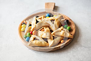 Assorted hamantaschen cookies and colorful candies on a wooden board on a gray background. Copy space