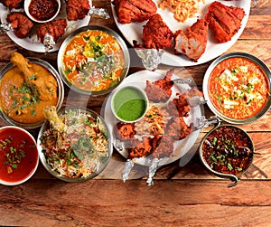 Assorted indian foods chicken biryani,chicken korma,chicken lollipop, paneer butter masala and tandoori chicken on wooden