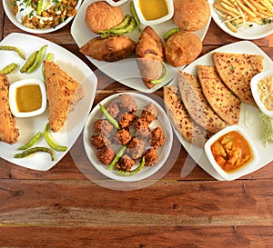 Assorted Indian Tea time snacks in group includes Spicy onion fritters, bread pakora,samosa, kachori and aloo paratha on wooden