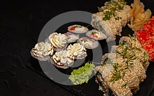 Assorted Japanese sushi on a black plate with wasabi and ginger