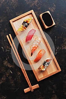 Assorted japanese sushi set on a wooden plate, dark stone background. Japanese sushi, soy sauce, chopsticks. Top view
