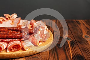 Assorted meat snacks on a wooden cutting board. Sausage, ham, bacon, smoked meats. Stock photo of meat products with blank space