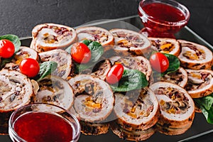 Assorted meat, stuffed chicken rolls, meat rolls stuffed with mushrooms, cranberries and dried apricots on black shale background