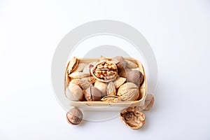 Assorted nuts in the shell on a white background: walnuts, pecans, almonds, macadamia. Nuts in a basket. Selective focus, close-up