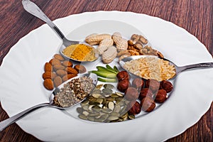 Assorted nuts in white bowl, plate on wooden surface. Top view with copy space