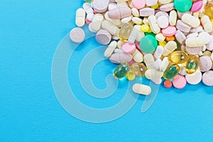 Assorted pharmaceutical medicine pills, tablets and capsules on blue background top view. Copy space