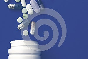 Assorted pharmaceutical medicine pills, tablets and capsules and bottle on blue background.