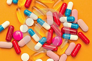 Assorted pharmaceutical medicine pills, tablets and capsules and bottle on orange background. Copy space for text