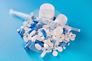 Assorted pharmaceutical medicine pills, tablets and capsules in bottle, syringe on blue background