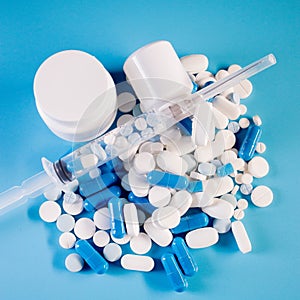 Assorted pharmaceutical medicine pills, tablets and capsules in bottle, syringe on blue background