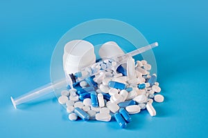 Assorted pharmaceutical medicine pills, tablets and capsules in bottle, syringe on blue background