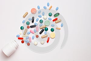 Assorted pharmaceutical medicine pills, tablets and capsules coming out of container over white background