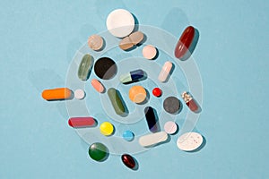 Assorted pharmaceutical medicine pills, tablets and capsules over blue background.