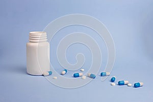 Assorted pharmaceutical medicine pills, tablets and capsules and white bottle on blue background. Copy space for text. Flat lay.