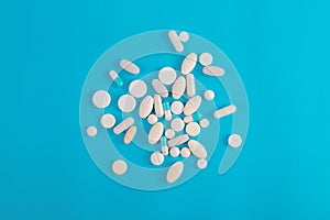 Assorted pharmaceutical medicine white  pills, tablets and capsules and bottle on blue background.