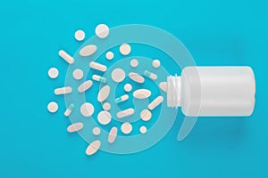 Assorted pharmaceutical medicine white  pills, tablets and capsules and bottle on blue background.