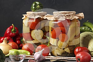 Assorted pickled cucumbers, patissons, peppers, zucchini and tomatoes in jars on a dark background, horizontal format