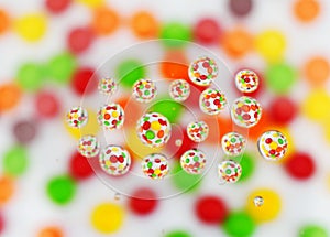 Assorted pieces of bright colorful round candy shot through water drops on white background