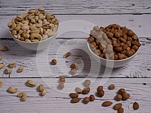 Assorted pistachio nuts, cashews, almonds and hazelnuts in two bowls on a white wooden table
