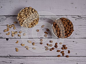Assorted pistachio nuts, cashews, almonds and hazelnuts in two bowls on a white wooden table top view