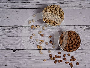 Assorted pistachio nuts, cashews, almonds and hazelnuts in two bowls on a white wooden table top view with copy space