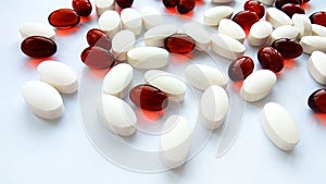 Assorted red and white pharmaceutical medicine pills, tablets and capsules on white background