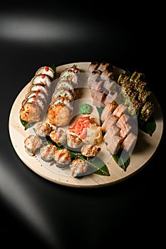 Assorted rolls including baked salmon and avocado on round board.