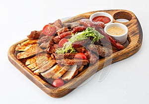 assorted sausages and meat with vegetables with mustard and ketchup on a wooden board isolated on white background