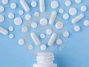 Assorted scattered pharmaceutical medicine pills, tablets and capsules and bottle on blue background. Medicine concept.