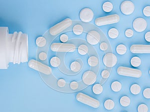 Assorted scattered pharmaceutical medicine pills, tablets and capsules and bottle on blue background. Medicine concept.