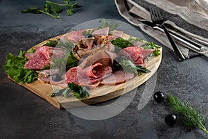 Assorted sliced delicious meat mix as salami, bacon and ham with parsley and olives on a wooden cutting board on grey cement