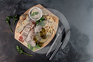 Assorted sliced delicious meat mix as salami, bacon and ham with pickles, lard and bread on a wooden cutting board on grey cement