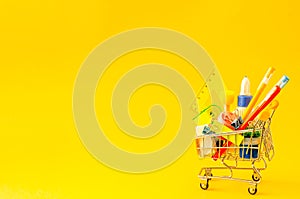Assorted stationery in a shopping trolley on a yellow background with place for text