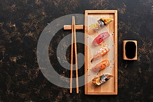 Assorted sushi set on a dark rustic background. Japanese food sushi on a wooden plate, soy sauce, chopsticks. Top view,copy space