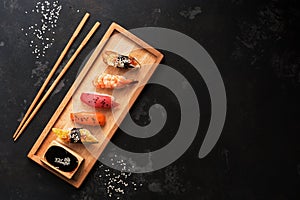 Assorted sushi set on a wooden plate, dark stone background. Japanese food sushi, soy sauce, chopsticks. Top view, copy space