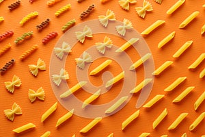 Assorted types of pasta organized on orange background. flat lay concept top view