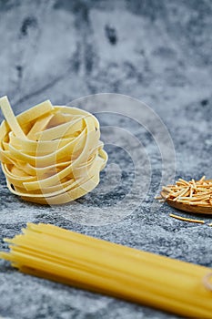 Assorted uncooked pasta on a marble background with a wooden spoon