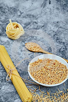 Assorted uncooked pasta on a marble background with a wooden spoon