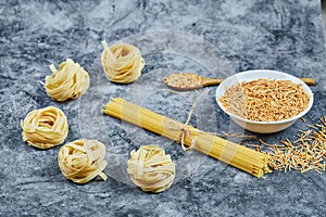 Assorted uncooked pasta on a marble background with a wooden spoon