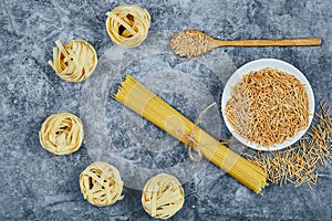 Assorted uncooked pasta on a marble background with a wooden spoon