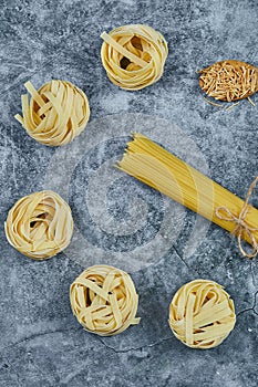 Assorted uncooked pasta on a marble background with a wooden spoon