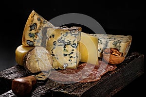 Assorted various gourmet cheeses and raw smoked sausages on a wooden board on a dark background. Various types of cheese: hard and