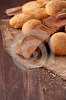 Assortement of bread on burlap on the wooden table. Slices of bread and roll.
