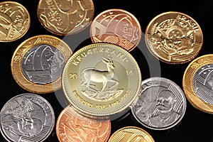 An assortment of Brazilian coins on a black reflective background with a South African one ounce gold Krugerrand coin