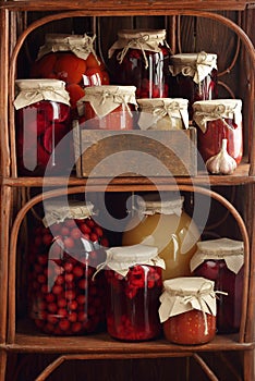 Assortment of canned preserves: fruit jam, compote, tomato paste and vegetable cans in the pantry on rustic wooden shelves